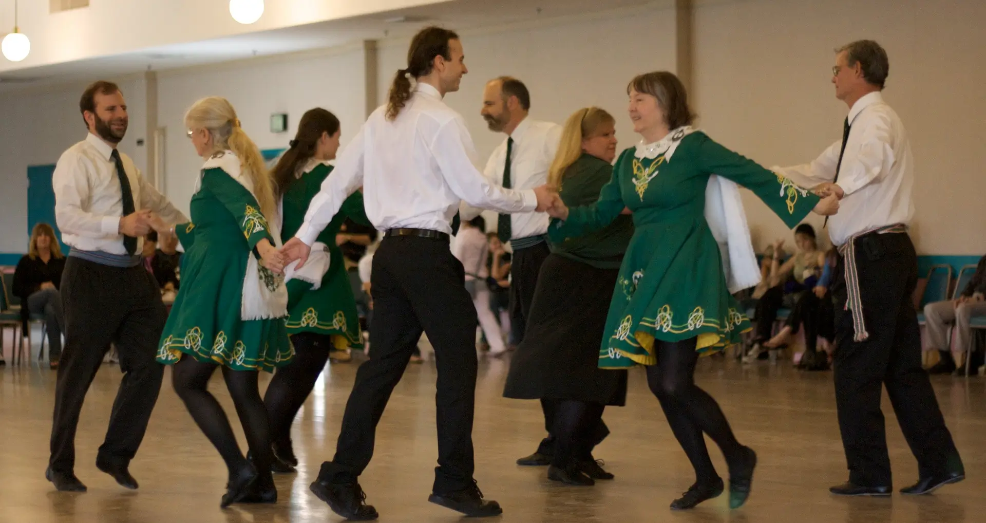 A group of performers wearing black, white, and green attire are dancing in a group while holding hands.