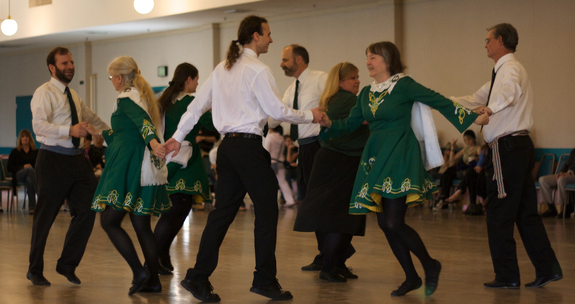 A group of performers wearing black, white, and green attire are dancing in a group while holding hands.