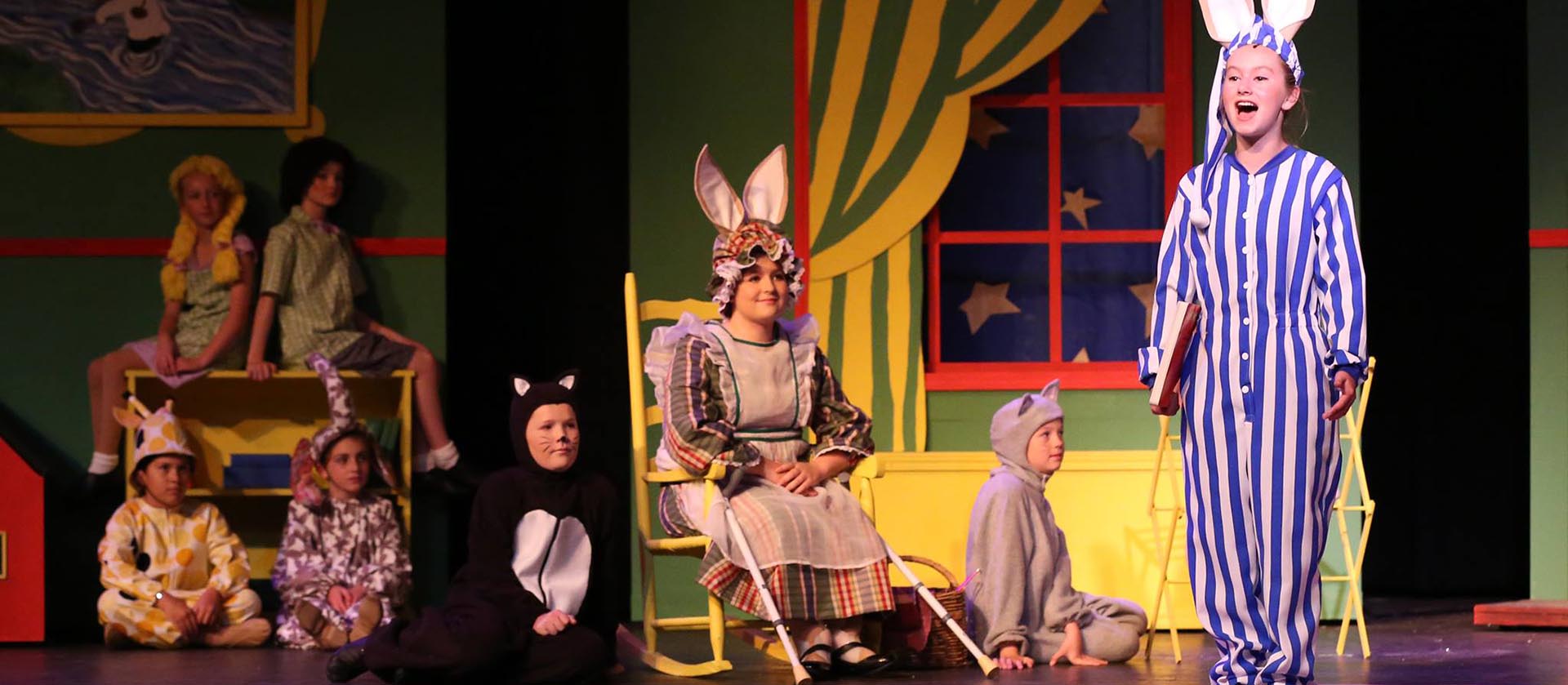 A group of young performers in costume performing a scene from Goodnight Mood.