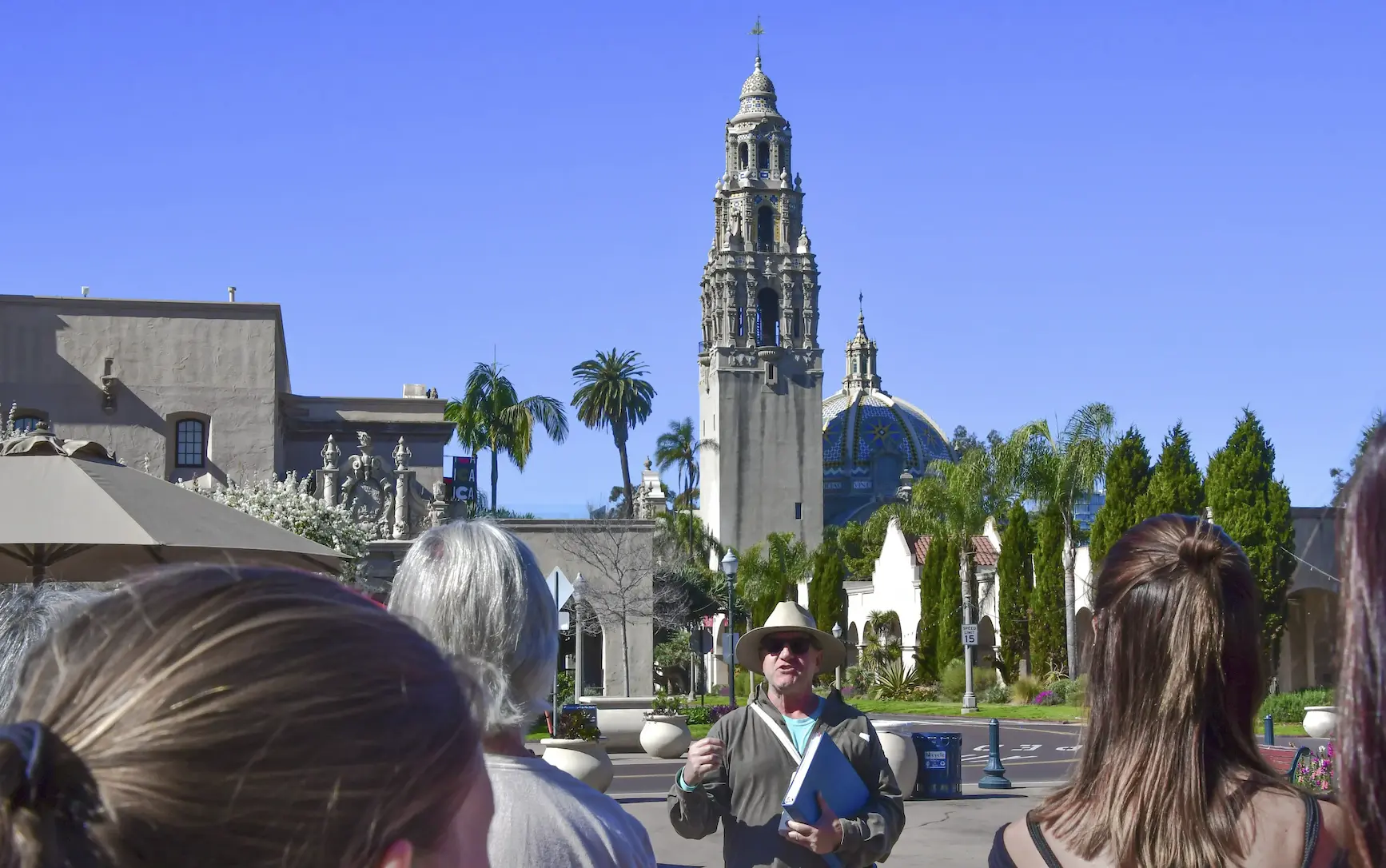 A tour group with the backs of park visitors heads in the foreground and the tour guide's face and California Tower in the background.