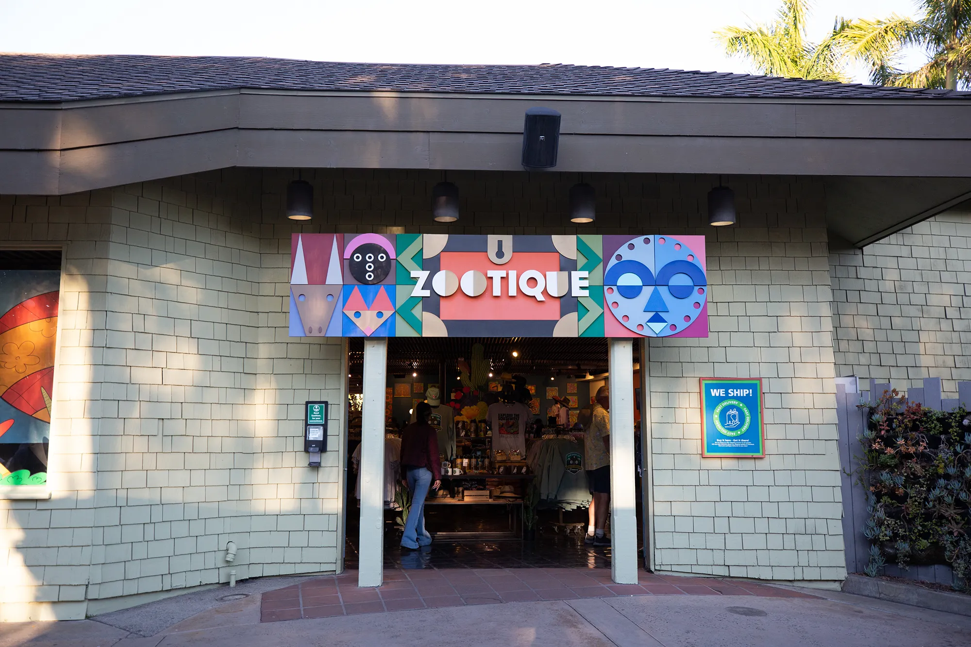 Entrance to the Zootique giftshop. A Zootique sign with colorful shapes is above the entry way. The building is white brick with a brown roof top.