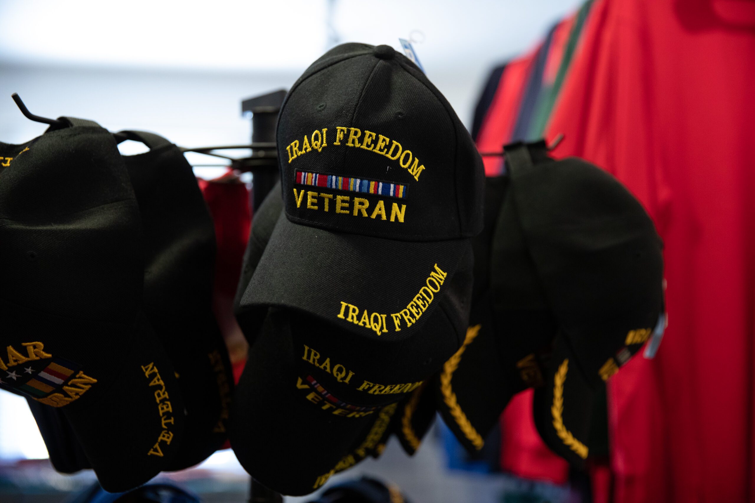 A Veterans Museum Gift Shop rack of black hats with yellow embroidered letters that says Iraqi Freedom Veteran on the brim and the front of the hat.