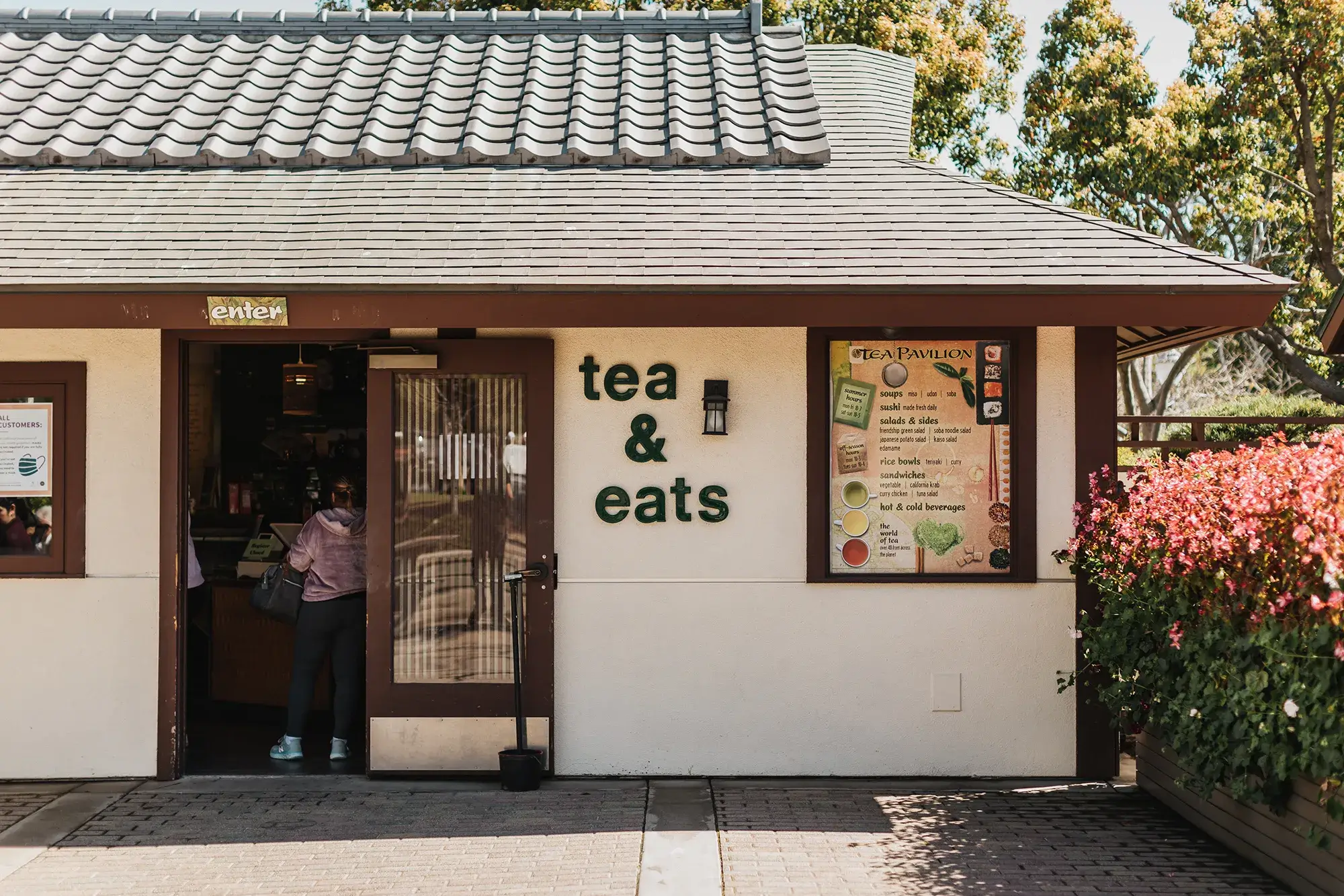 Front entrance to the Japanese Friendship Garden's Tea Pavilion. The building is beige with brown trim and a roof.