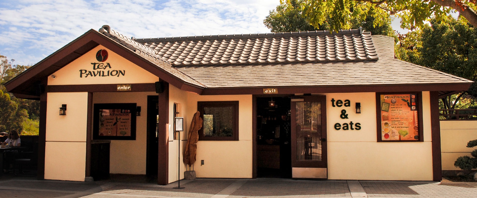 Front entrance to the Japanese Friendship Garden's Tea Pavilion. The building is beige with brown trim and a roof.