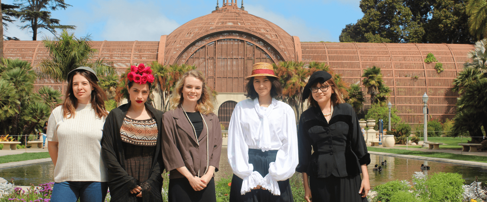 A group of people dressed as important women in women's history standing in front of the lily pond and the Botanical building.