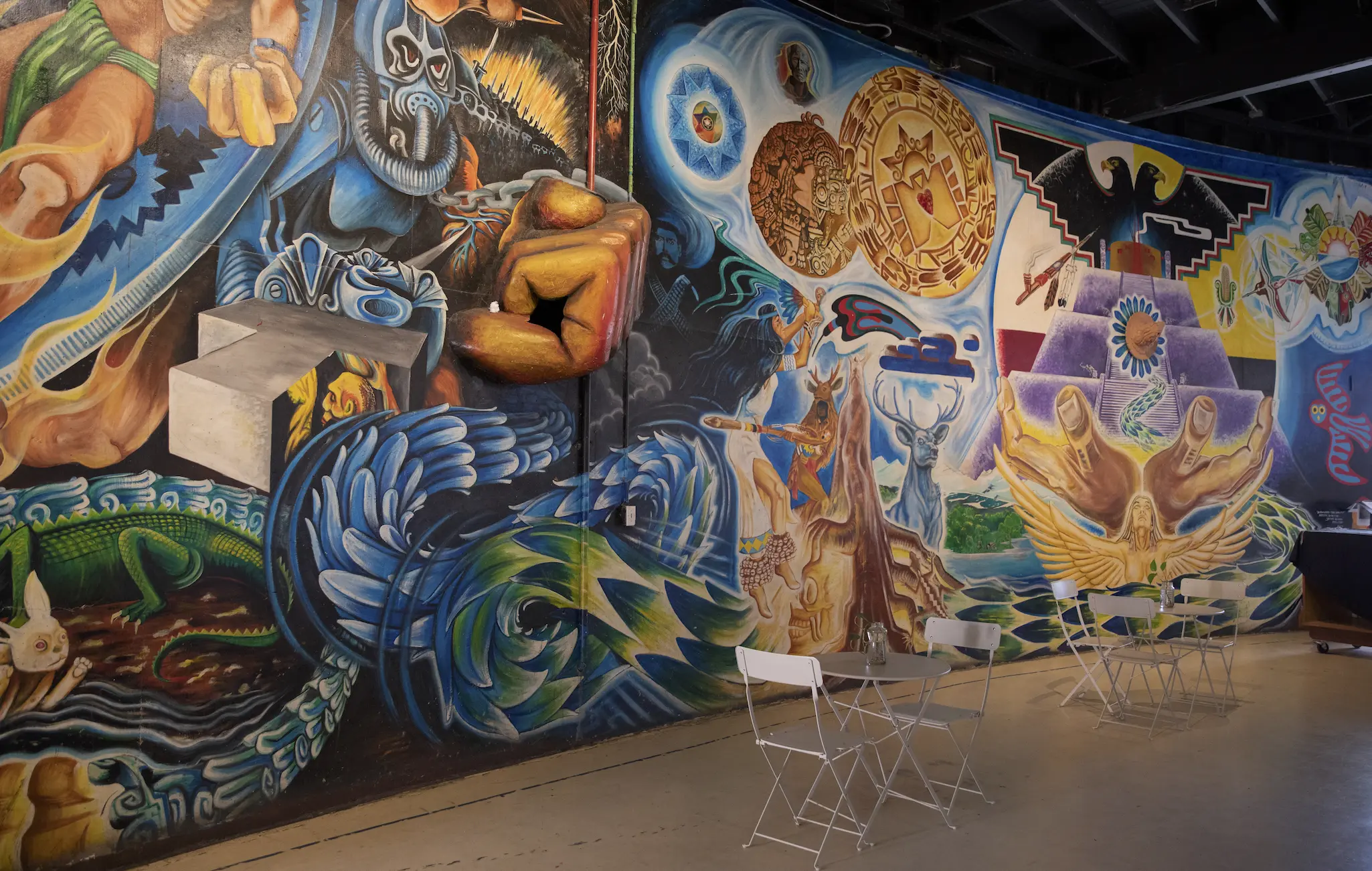 Colorful murals inside Cultural de la Raza's building depicting animals, hands and symbols.