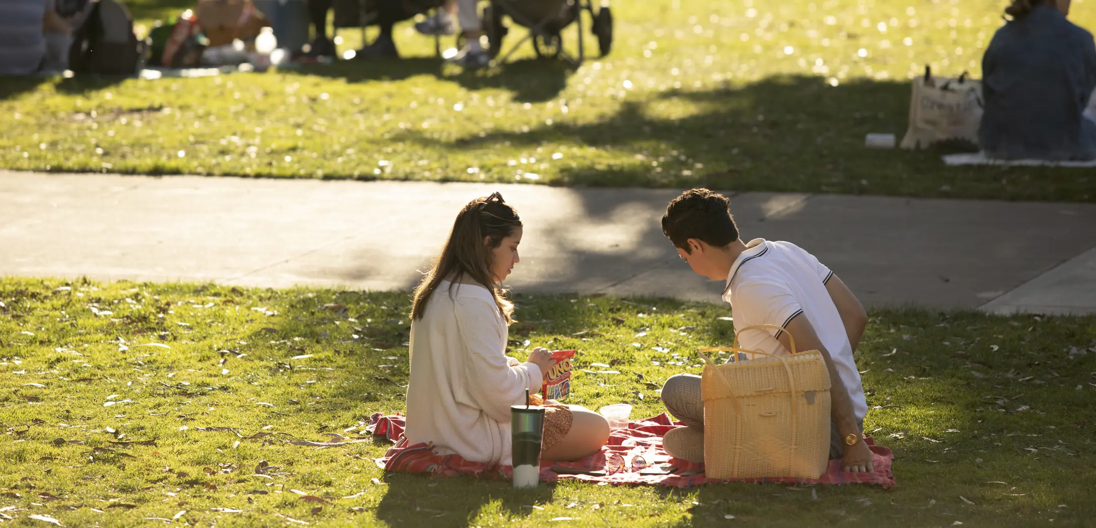 Two young adults sitting on a red blanket outdoors playing the card game Uno.