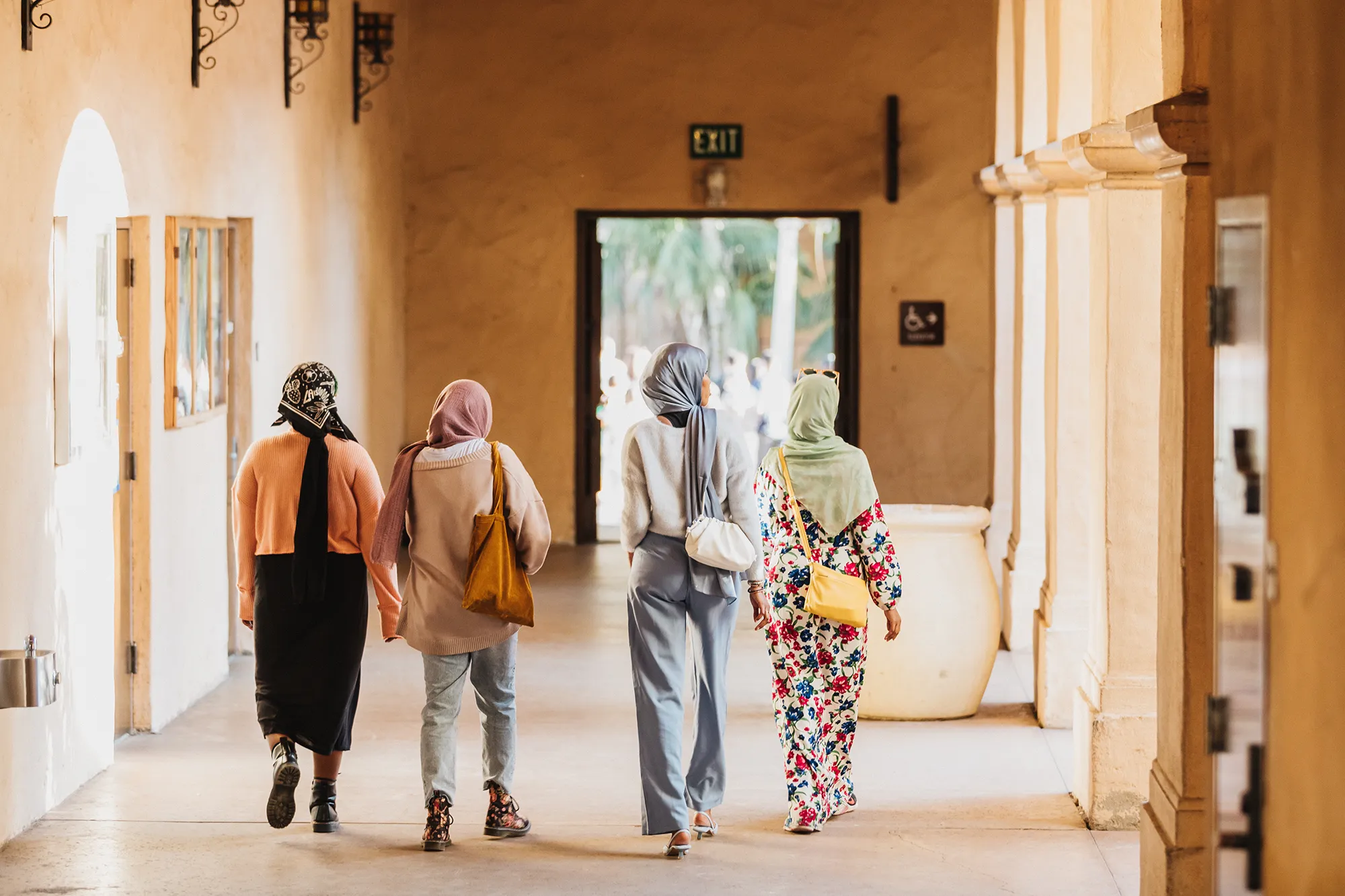 Four people with head-coverings walking down a hallway in Balboa Park.