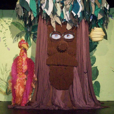A brown tree trunk with eyes and a mouth. A red bird stands next to it.