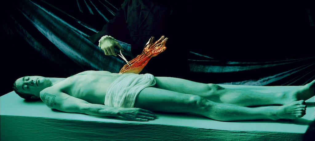 Male body laying on a table with one arm held up. It appears to be metal or golden and another person is inspecting it.