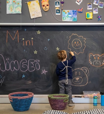 child drawing on a chalkboard with mini mingei written on it
